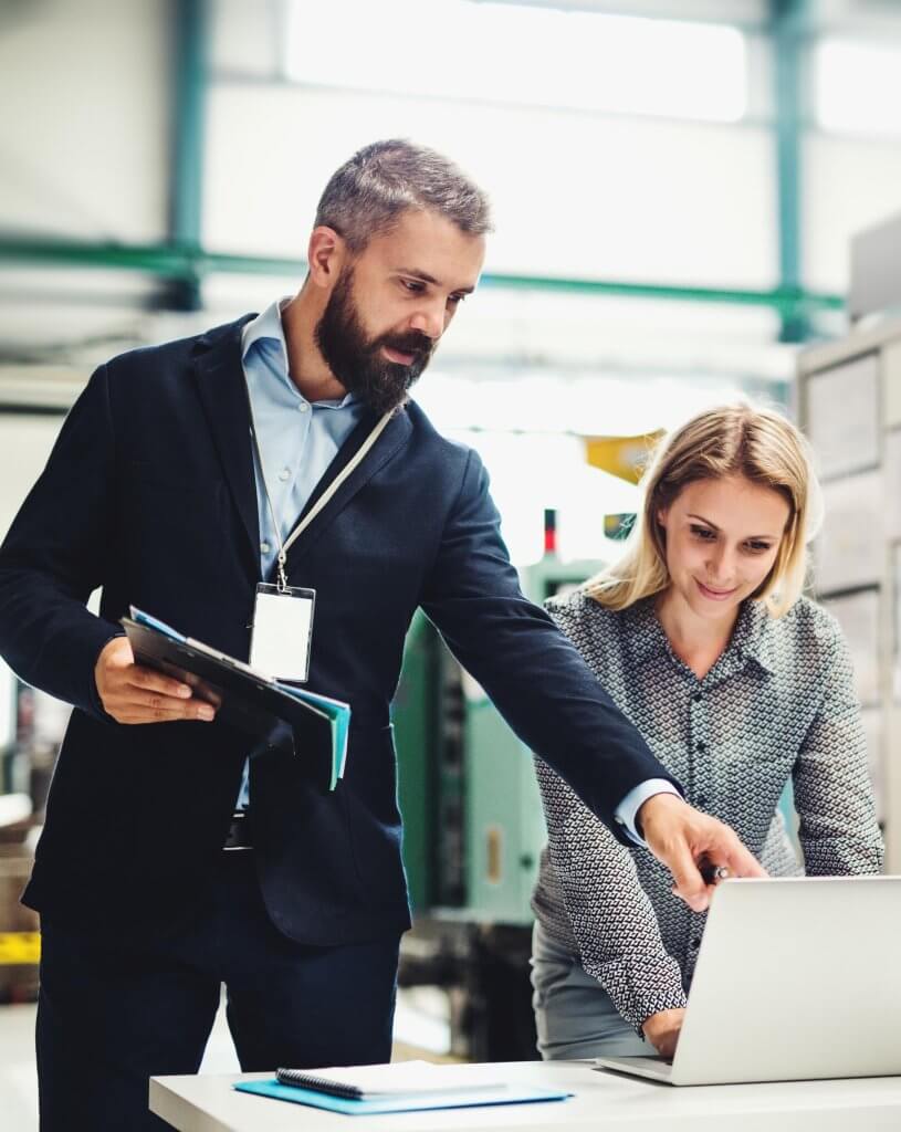 A portrait of a serious mature industrial man and woman engineer with laptop in a factory, working.